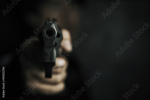 Threat of firearms. Muzzle of gun in man's hand is pointed at camera. Male criminal holds revolver on black background. Attack or defense.