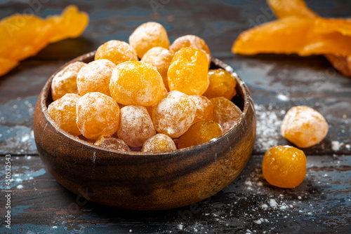 Candied citrus fruits with powdered sugar in a wooden bowl on a dark background. Candied kumquat.