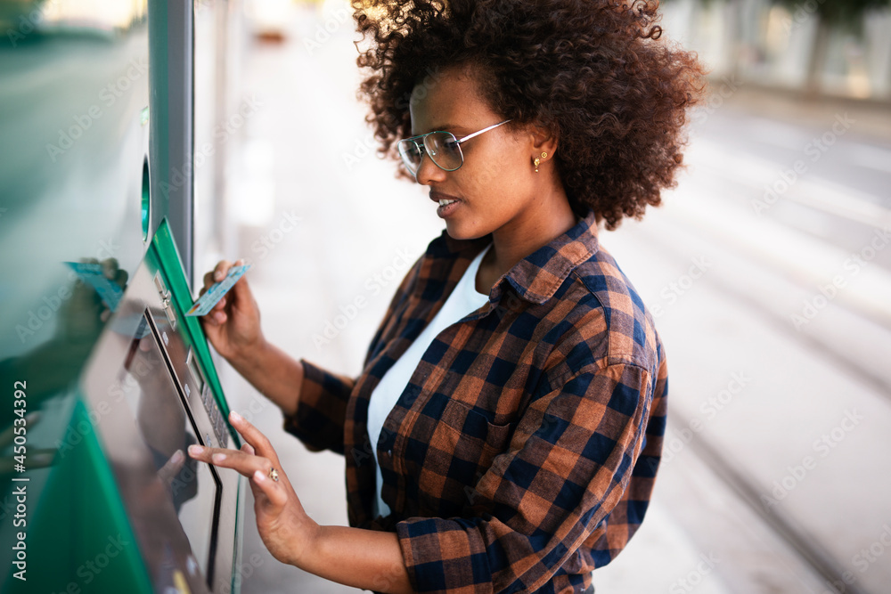 Beautiful African woman using ATM machine. Attractive young woman withdrawing money from credit card at ATM..