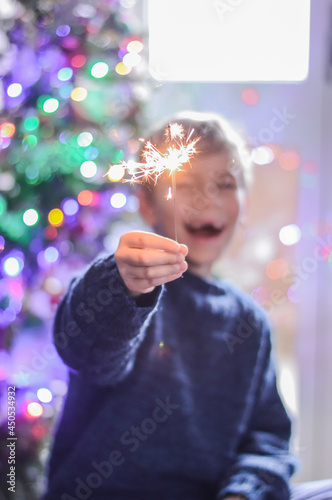 selective focus happy boy is holding a burning sparkler on festive lights background