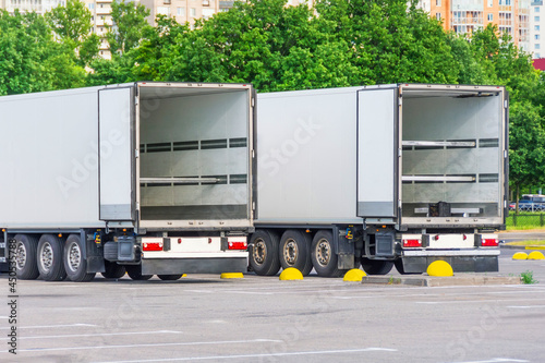 Cuadro en lienzo Two trucks in a parking lot with an empty container trailer open gates at the back, ready to load products, goods cargo