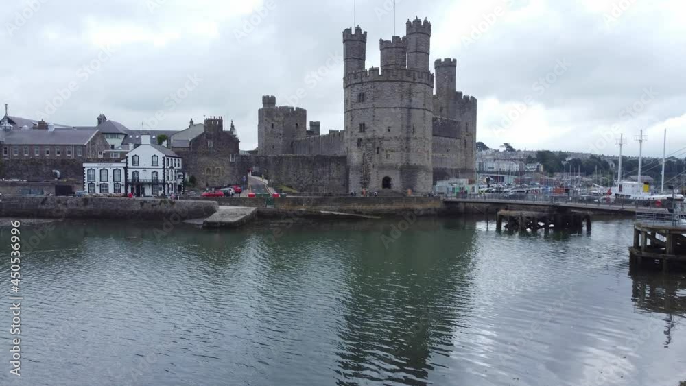 Ancient Caernarfon castle Welsh harbour town aerial view medieval waterfront landmark low left rising shot Ancient Caernarfon castle Welsh harbour town aerial view medieval waterfront landmark low left rising shot