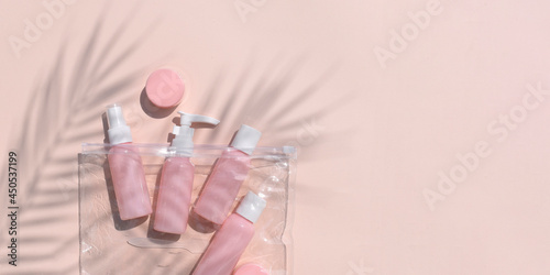 Minimal flat lay with pink beauty products bottles bag on neutral background. Summer cosmetic still life concept for womens travelling, skin or body care treatment for trip. Mockup trendy palm shadows