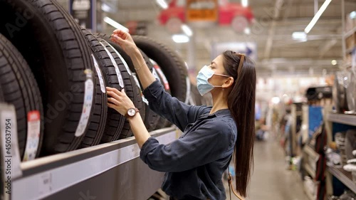 Young focused woman in face medical mask examaning brand and product characteristics while buying new tires photo