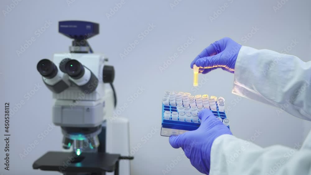 A medical scientist take out and examine small test tubes of vaccines against the backdrop of laboratory equipment A medical scientist take out and examine small test tubes of vaccines against the backdrop of laboratory equipment