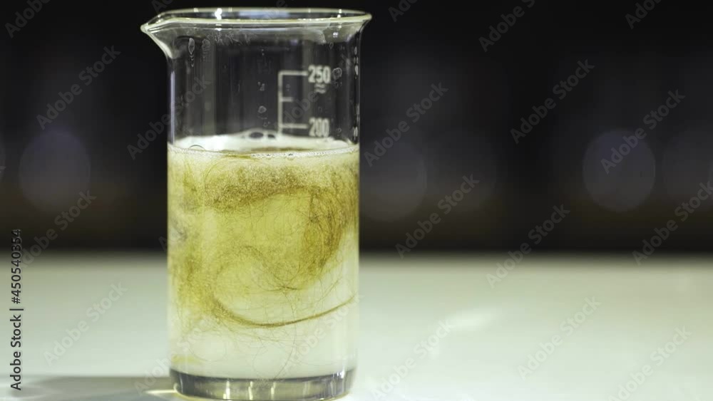 A glass flask with a yellow chemical liquid that dissolves hair close-up A glass flask with a yellow chemical liquid that dissolves hair close-up