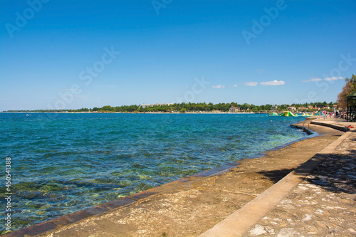 Tourists and locals enjoy the summer sun and sea on the coast just north of the historic centre of Porec on the Istria coast of Croatia 