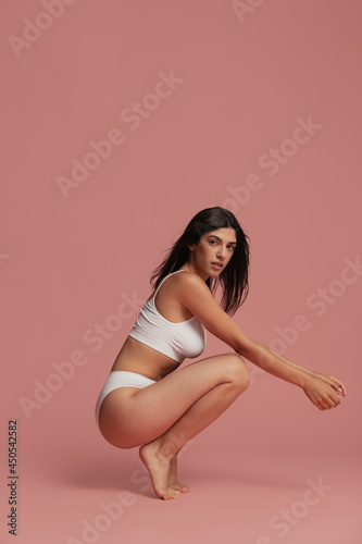 Portrait of young beautiful slim woman in lingerie posing isolated over pink studio background. Natural beauty concept.