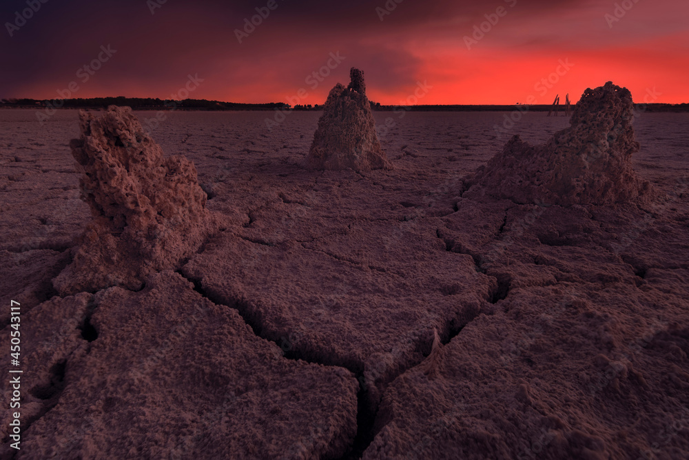 Fototapeta premium Dry lagoon landscape with cracked formations and reddish-colored cloudy skies, Toledo, Spain.