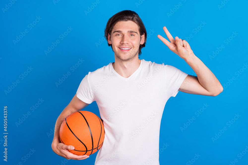 Photo of young happy positive cheerful man hold hands basketball make v-sign isolated on blue color background
