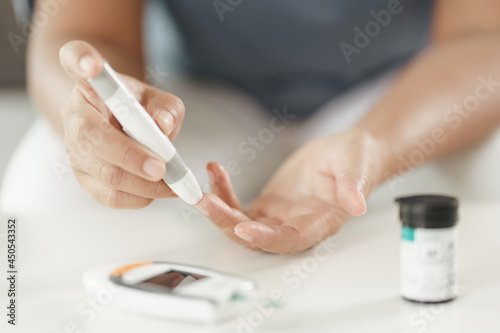 Mature Asian woman using lancet on finger for checking blood sugar level by Glucose meter, Healthcare and Medical, diabetes, glycemia concept
