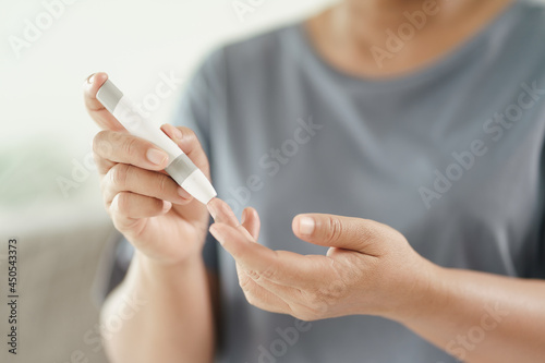 Mature Asian woman using lancet on finger for checking blood sugar level by Glucose meter  Healthcare and Medical  diabetes  glycemia concept