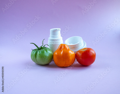 Cream and mask for skin care in white jar and tube with dispenser near bright juicy tomatoes. Concept Useful Natural Cosmetics from Tomato with Vitamins and Antioxidants.