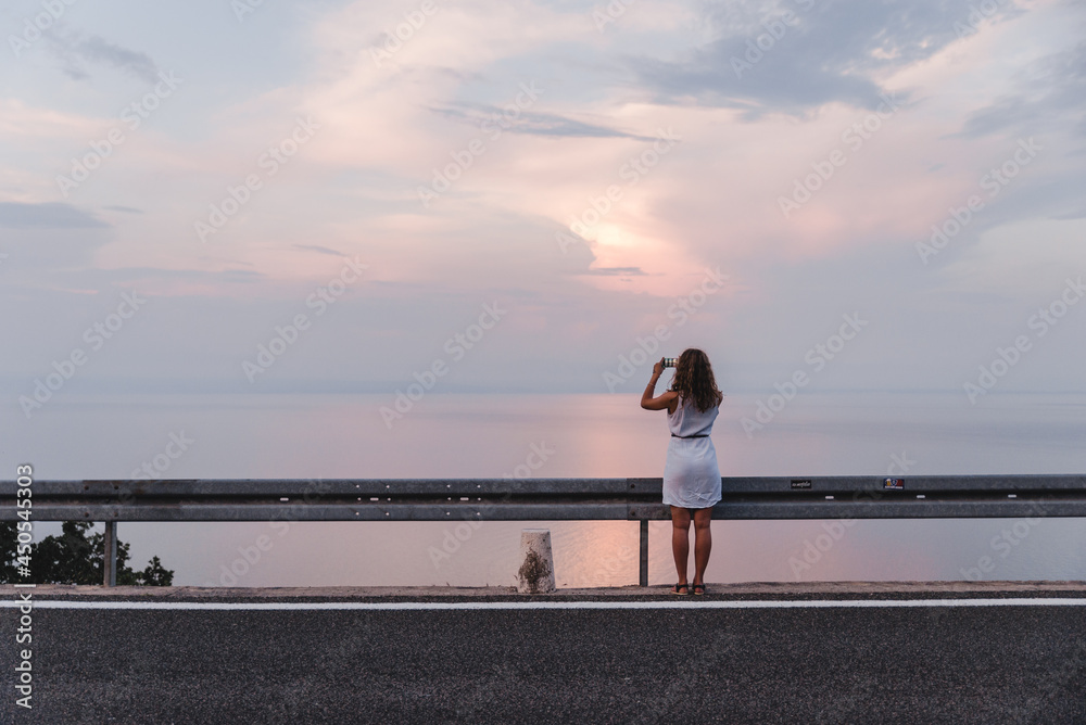 stop on the road woman taking picture on the phone of sunset above the sea