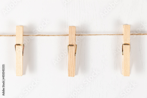 three wooden clothespins with a metal spring hang on a rope on a white background. selective focus