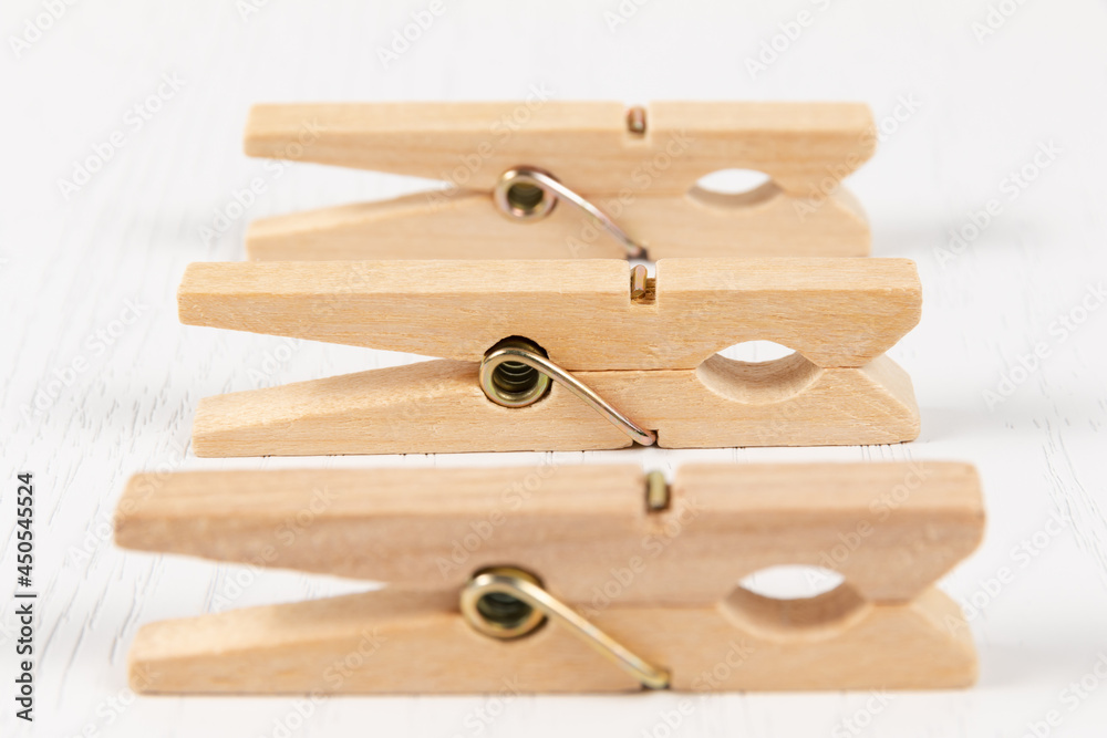 three wooden clothespins with a metal spring on the background of a white wooden table. close-up. selective focus three wooden clothespins with a metal spring on the background of a white wooden table. close-up. selective focus