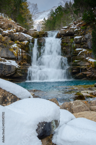 Waterfall in mountain river landscape in snowy winter, with trees at Pyrenees, national park, Spain