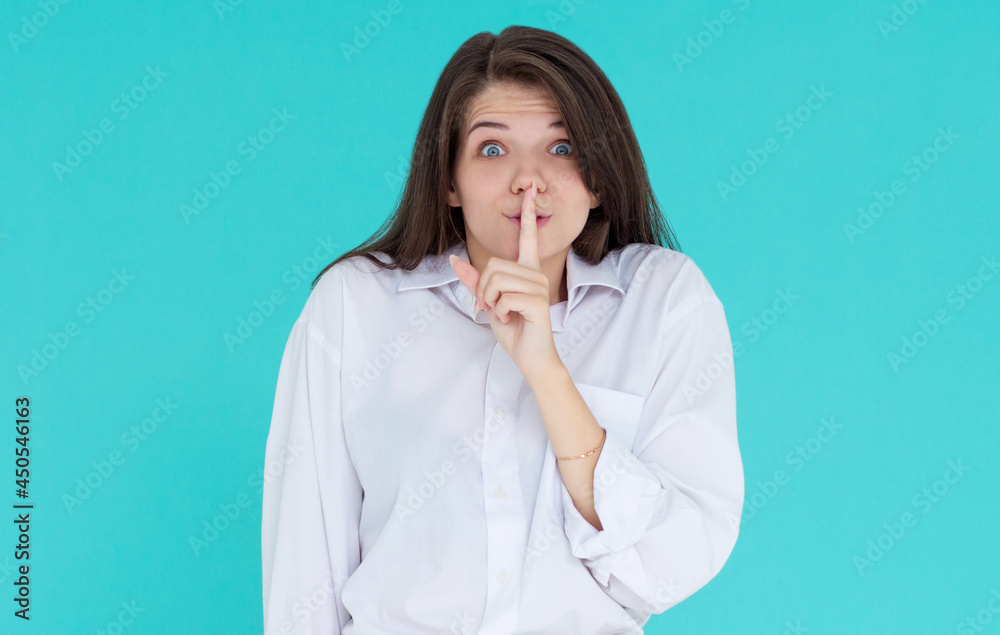 Pretty charming young woman having secret while holding finger on lips and showing silence sign while standing on blue background Pretty charming young woman having secret while holding finger on lips and showing silence sign while standing on blue background