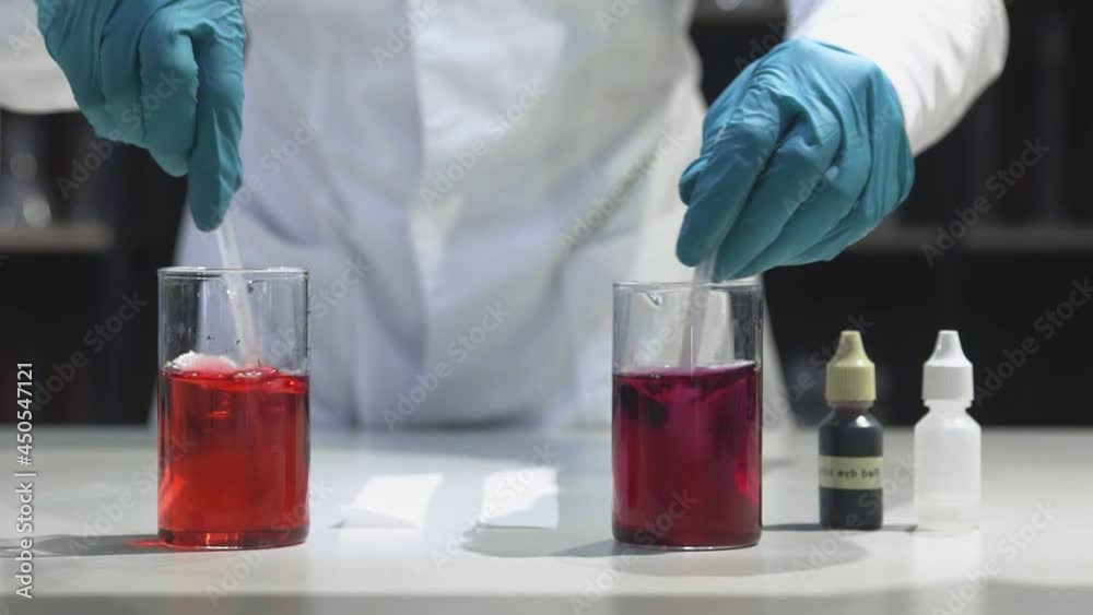 A male chemist in the laboratory mixes a red liquid in glass cones A male chemist in the laboratory mixes a red liquid in glass cones