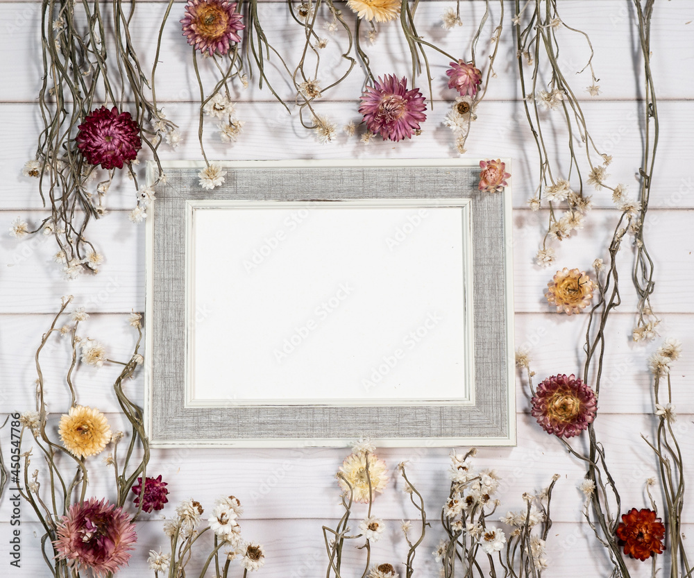Top view of empty photo frame with dry colorful flowers over a white wooden table - obrazy, fototapety, plakaty 