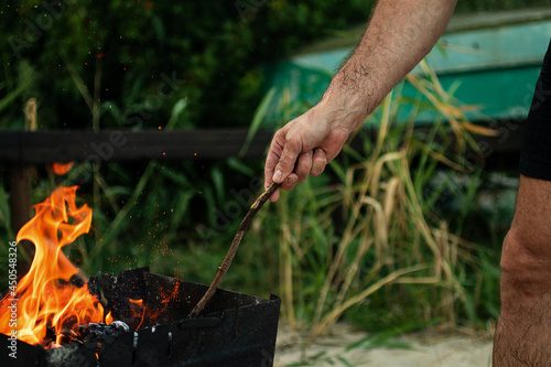 A man holds a stick in his hands and kindles fire in nature.Concept of outdoors picnic.