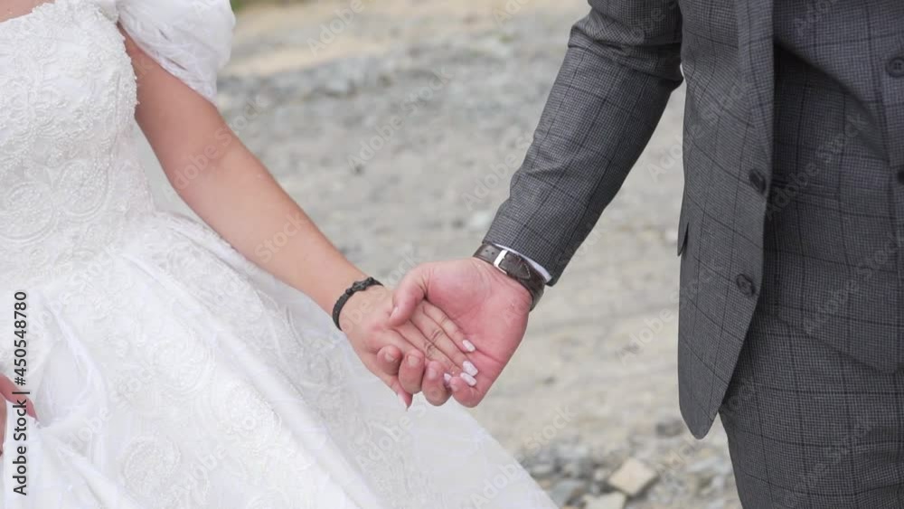 Brideand groom in wedding clothes hold hands and the husband goes forward and pulls his wife by the hand. Relationships between spouses. Wedding day. Love relationship between a man and a woman. Brideand groom in wedding clothes hold hands and the husband goes forward and pulls his wife by the hand. Relationships between spouses. Wedding day. Love relationship between a man and a woman.