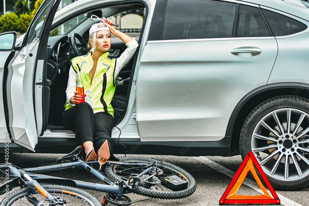 girl in emergency vest in the car drinks beer. the bike lies on the asphalt girl in emergency vest in the car drinks beer. the bike lies on the asphalt
