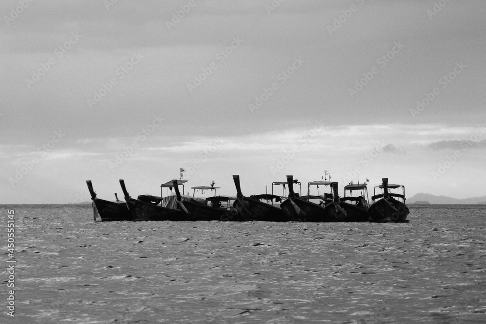 Group of wooden long tail boat floating on sea with raining cloud background in black and white tone or monochrome. Transportation and Nature of Thai ocean at Krabi, Thailand. Art Picture style 