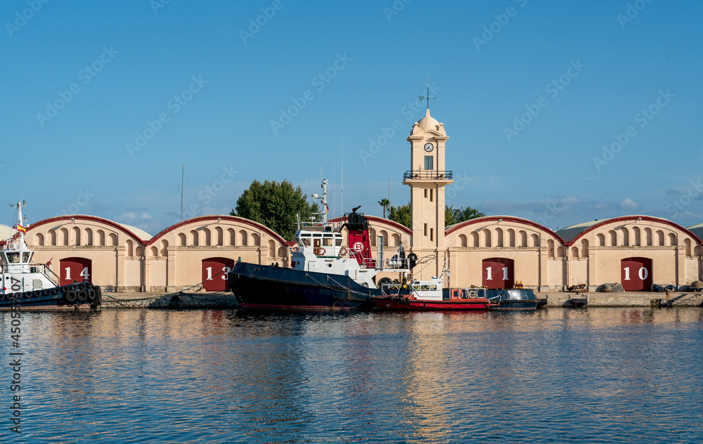 Boats in front of warehouses and lighthouse at the port of Gandia, Spain