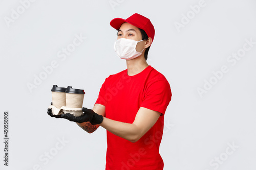 Here is your order, have nice day. Friendly smiling delivery man, fast-food employee, extend hands and give coffee cups to client, wear protective gloves and medical masks. Courier bring bevereges photo