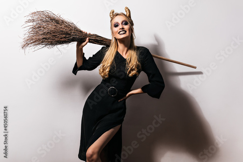Shapely female vampire posing with black makeup. Attractive witch with broom chilling at halloween party.