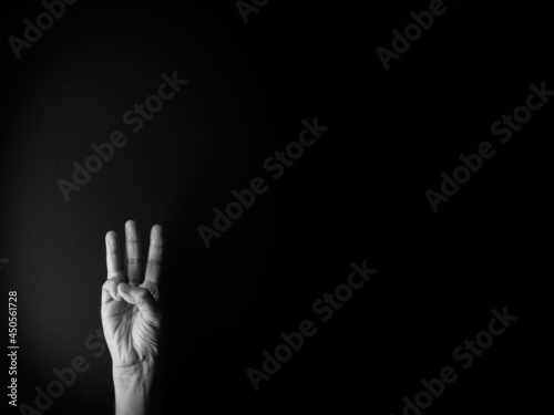 Black and white image of hand demonstrating sign language number three against black background with empty copy space