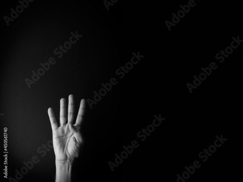 Black and white image of hand demonstrating sign language number four against black background with empty copy space