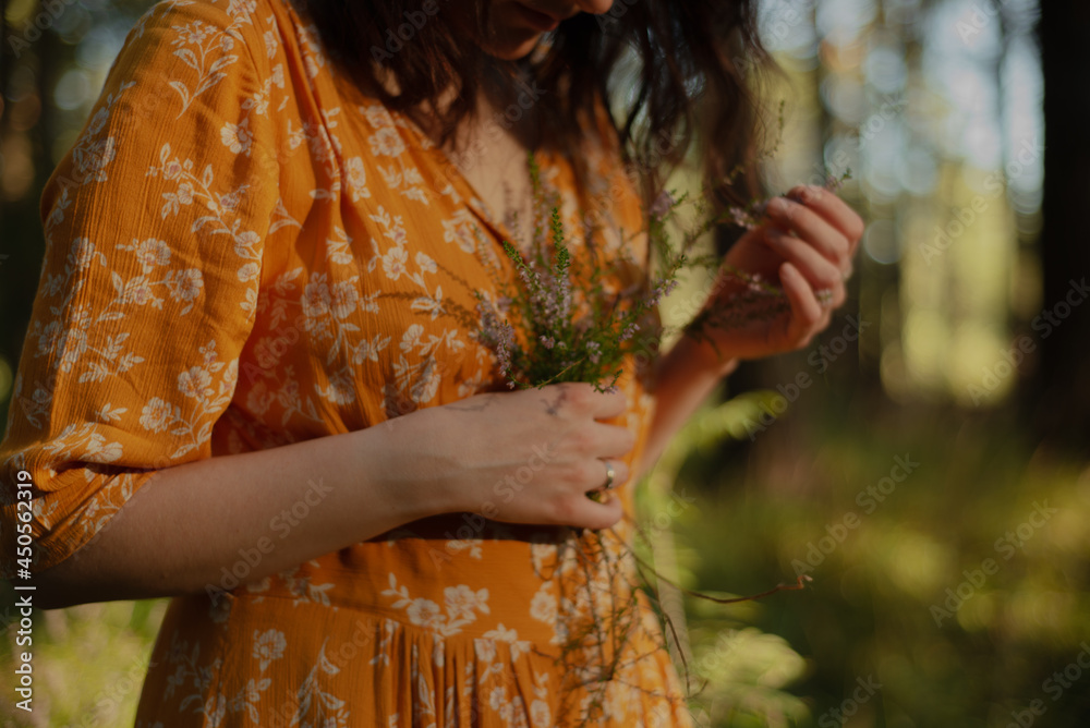a beautiful girl in a yellow dress stands in the forest in summer and holds a bouquet of flowers in her hands.