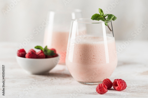 Two glasses with a Lassi drink with raspberries, mint and a bamboo tube on a light background.