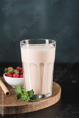 Lassi drink with raspberries in a glass with mint and a bamboo tube on a wooden board.