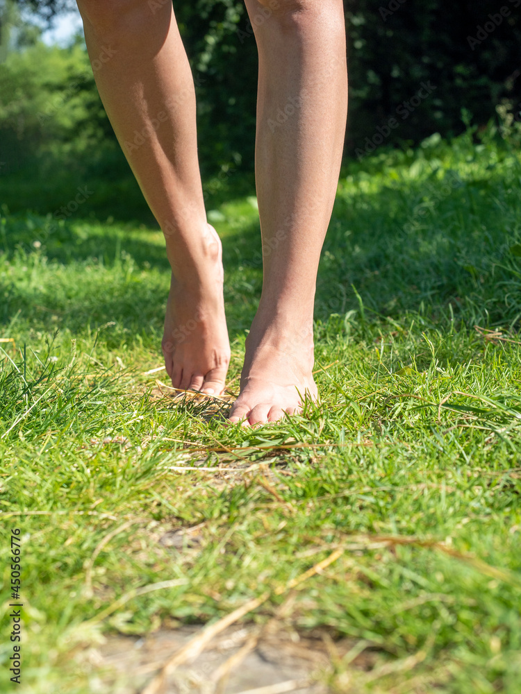 Close-up of elegant female legs walking barefoot on the green grass in summer