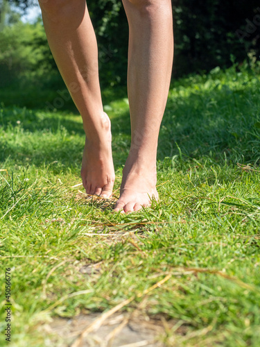 Close-up of elegant female legs walking barefoot on the green grass in summer