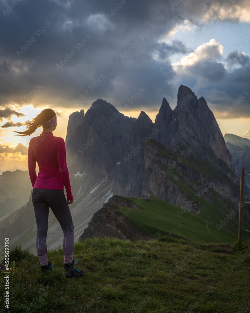 a woman standing on top of mountain watching a sunrise behind beautiful rock formation Seceda 