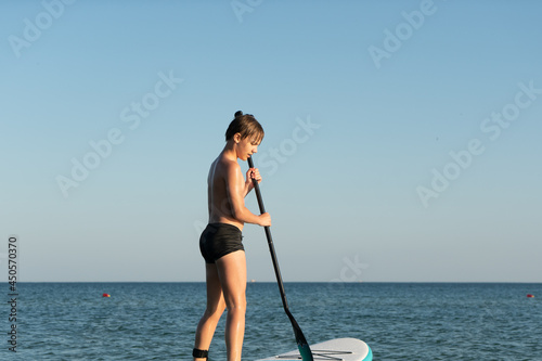 A 12 year old boy learns to stand on a SUP board in the sea near the shore. photo