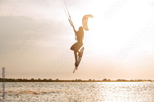 Young woman professional kiter performs a difficult trick in the air on a beautiful background of the sunset and sea