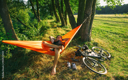 Bike traveler resting in the hammock after long day riding bicycle packed by bags at sunset