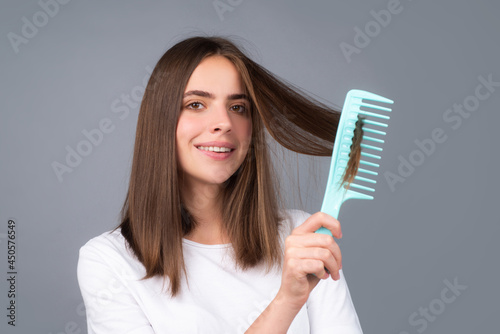 Smiling girl combing hair. Beautiful young woman holding comb straightened hair. Attractive smiling woman portrait with comb.