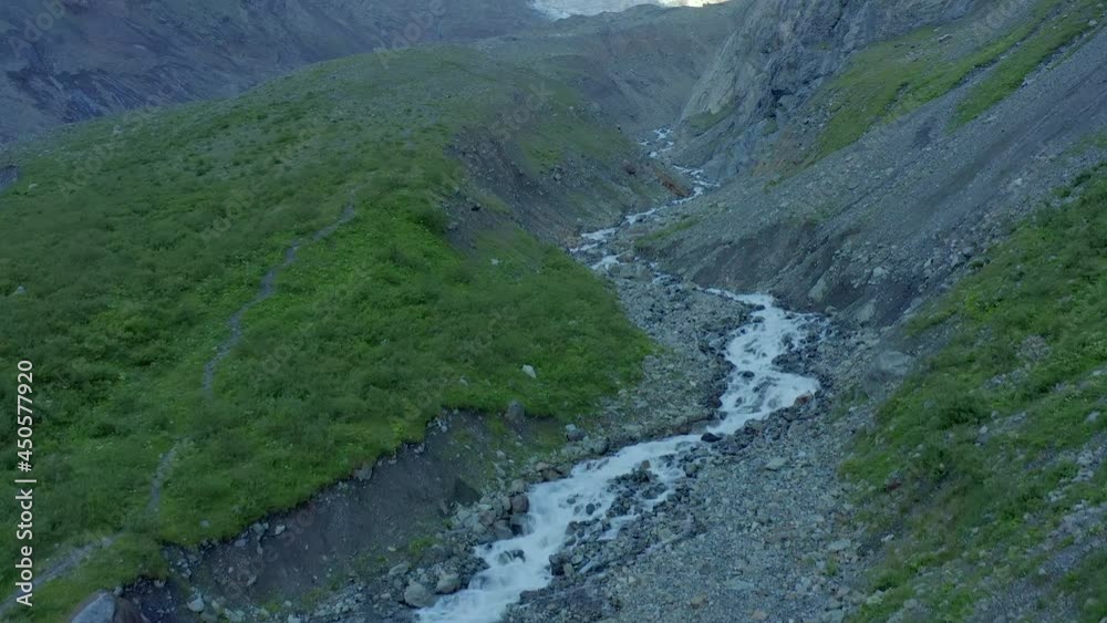 Aerial view of the source of a mountain river in the mountains, rocks and a snow-capped peak in front. Aerial view of the source of a mountain river in the mountains, rocks and a snow-capped peak in front.