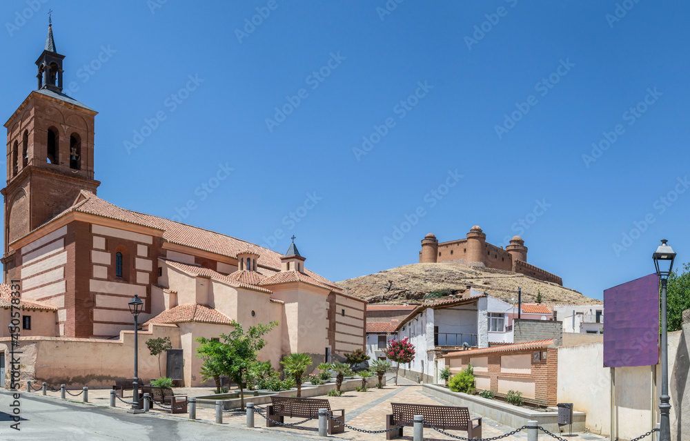 panoramic view of the church square of the town of La Calahorra with a fountain, plants, benches and the castle of La Calahorra in the background on the hill