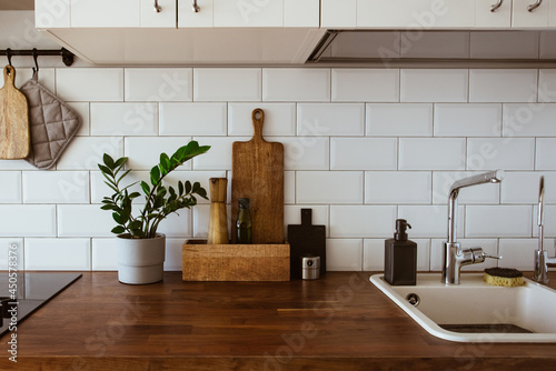 Kitchen brass utensils, chef accessories. Hanging kitchen with white tiles wall and wood tabletop.Green plant on kitchen background
