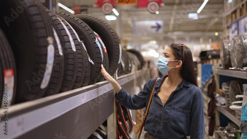 Young focused woman in face medical mask examaning brand and product characteristics while buying new tires photo