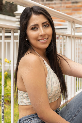 Free Download attractive young woman with her long black hair sitting and leaning to a railing, happily wears a jean, gray casual top and natural makeup, lifestyle and fashion - GFXLoad