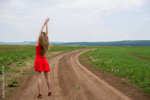 a girl in a red dress on the field raised her hands up photo from the back