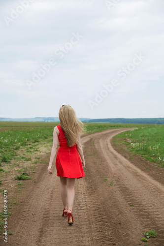 a blonde in a red dress walks across the field in shoes photo from the back